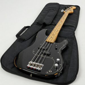 A person carefully placing an electric bass guitar into a hard-shell case with foam inserts.