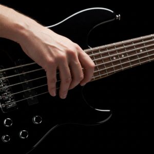 Close-up of a hand using fingerstyle technique on the strings of a 5 string electric bass guitar.