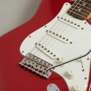 Detailed view of the chrome tremolo bridge and white pickguard on a red fender stratocaster.